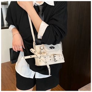 Détail du sac bandoulière blanc cassé avec boucle de ceinture et œillets argentés punk