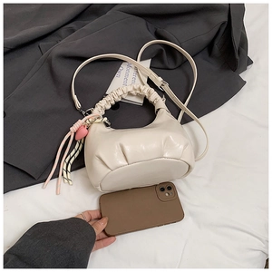 Close-up of off-white ruched crescent handbag with heart charm and phone for scale