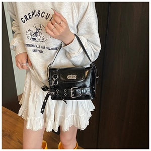 Détail d'un sac bandoulière en cuir verni noir avec boucle argentée et accents métal