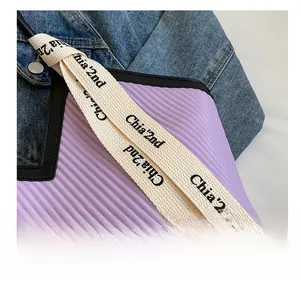 Détail du sac plissé violet avec bandoulière beige tissée et texte de la marque