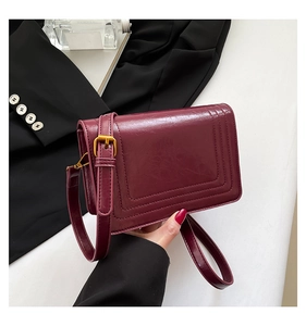 Detail of burgundy crossbody bag with U-shaped stitching and gold-tone hardware