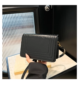 Detail of glossy black square crossbody bag with crackle texture and golden buckle