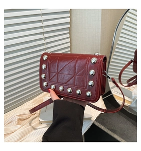 Detail of red-brown square crossbody bag with silver rivets and quilted geometric design