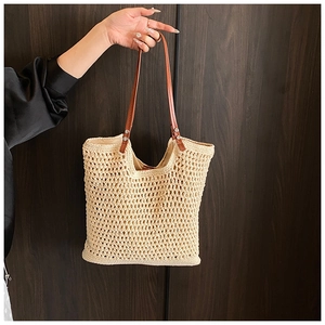 Close-up of beige hollow-out woven straw tote with brown leather handles and metal rivets