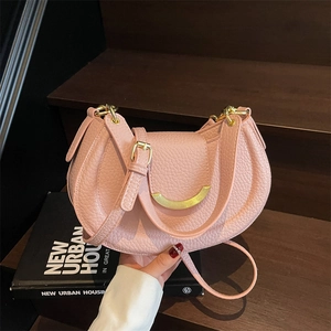 Pink crescent moon shoulder bag with textured leather and gold hardware in urban setting