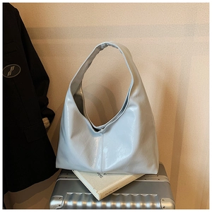 Détail du grand sac cabas bleu clair en cuir froissé brillant sur une valise