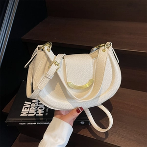 Minimalist white lychee leather crescent saddle bag with gold metal hardware on wooden stairs