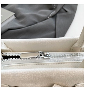 Close-up of smooth silver zipper and premium lychee grain white leather texture on tote bag