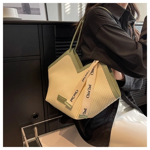 Détail du sac cabas plissé crème avec bordure verte porté par un mannequin chic