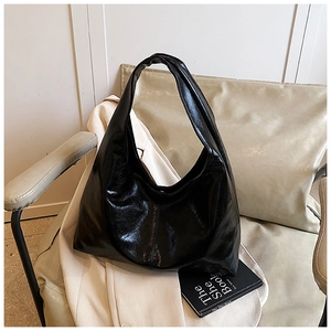 Détail d'un sac hobo en cuir brillant noir avec plis naturels sur un fauteuil beige