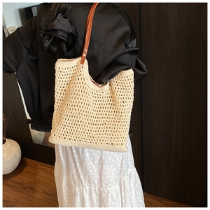 Detail of beige hollow crochet tote bag with brown leather strap worn by a model