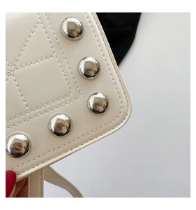 Detail of white quilted leather bag featuring large silver metal rivets and stitching