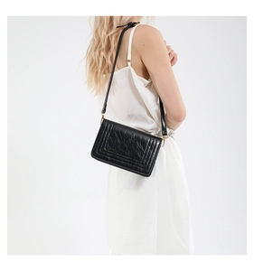 Detail view of black oily faux leather shoulder bag texture with stitching and strap