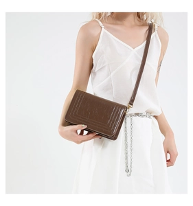 Detail of a brown patent leather crossbody bag showing glossy texture and shoulder strap