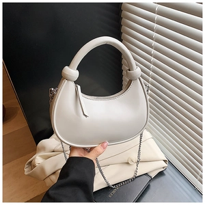 Close-up of cream half-moon bag with elegant leather knot detail and silver chain strap