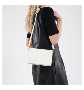Detailed side view of a white quilted leather crossbody bag worn by a fashion model