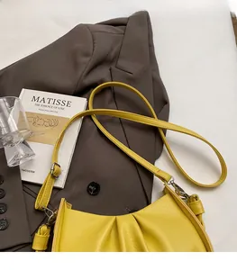 Close-up of bright yellow pleated bag with adjustable silver strap and moon shape