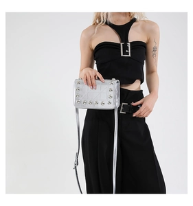 Detail of silver metallic crossbody bag with rivets shown on a black and white outfit