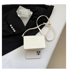 Close-up of white leather square bag featuring rectangular quilted lines on a black suit