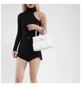 Detail of white faux leather tote bag with lychee texture and buckle strap on black outfit