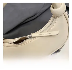 Detail show of silver zipper and knotted handle on beige crescent shoulder bag