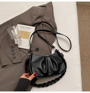 Detail of black pleated cloud bag with braided handle on minimalist white background