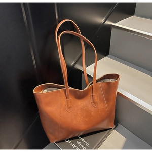 Detail of caramel brown leather tote bag showing smooth texture on a modern staircase