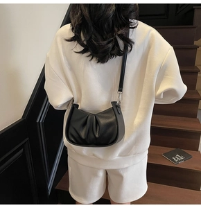 Detail of black pebbled leather crossbody bag with ruching and adjustable shoulder strap
