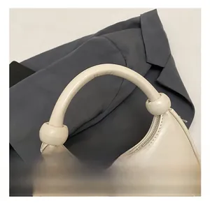 Detail of a creamy white crescent bag featuring a thick round handle and metal ball buckle