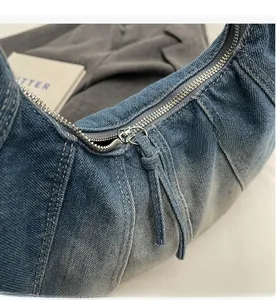 Detail of a smooth silver metal zipper on a blue denim shoulder bag with a long fabric puller