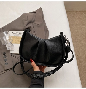 Detail of black pleated crescent bag with woven strap and smooth leather texture