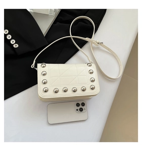 Detailed view of white quilted crossbody bag with silver studs and a smartphone for scale