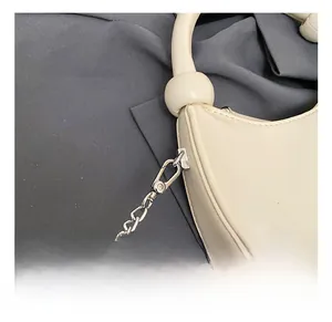 Detail of silver metal hook and chain hardware on cream semi-circular handbag