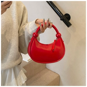 Detail of red crescent handbag showing knotted handle texture and silver D-ring hardware