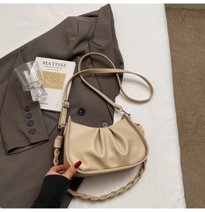 Detail of beige pleated crescent bag with braided strap on dark gray suit jacket