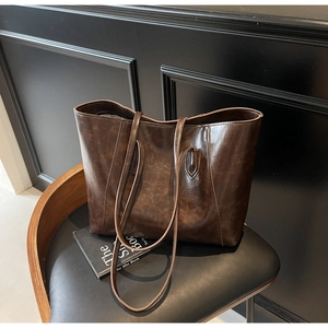 Close-up of vintage dark brown faux leather tote bag with glossy finish on chair