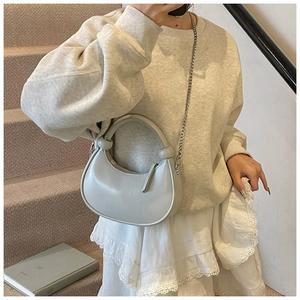 Model wearing a light grey half-moon handbag with a silver chain strap and knot detail
