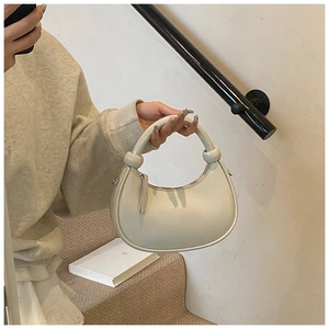 Close-up of beige hobo bag with knotted handle detail held by model on minimalist stairs
