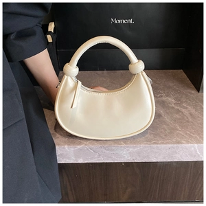 Detail of cream white half-moon handbag with knot handles on a marble surface