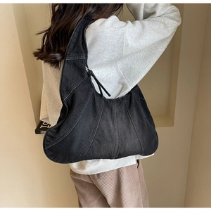 Close-up of black denim crescent bag with patchwork stitching and metallic zipper