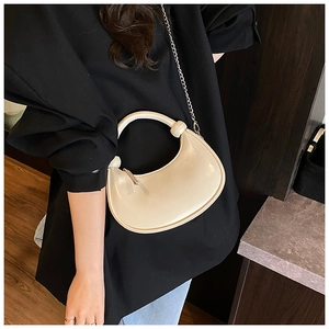 Detail of cream crescent leather bag with silver chain worn over a black outfit