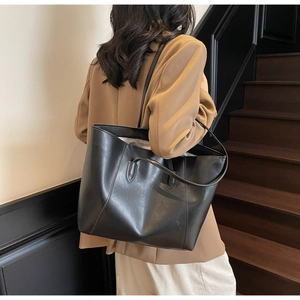Detail of large black glossy leather tote bag with slim shoulder strap on a model