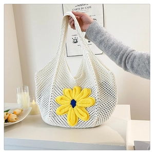 Detail of white crochet tote bag with large yellow knit flower in a cozy indoor setting
