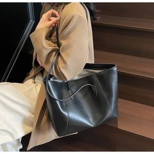 Detail of minimalist black tote bag showing smooth PU leather texture and side stitching