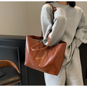 Detail of deep brown faux leather tote bag with dual straps worn by a model in casual style