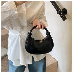 Detail of minimalist black glossy half-moon bag with decorative knotted handle design