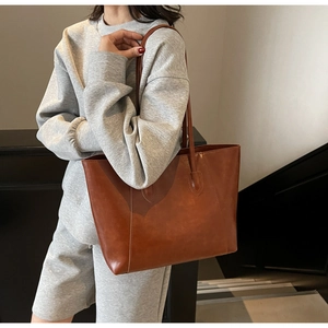 Close-up of a large brown leather tote bag worn by a model in a minimalist setting