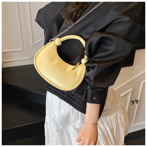Detail of yellow round handbag with silver chain strap worn with a black satin shirt