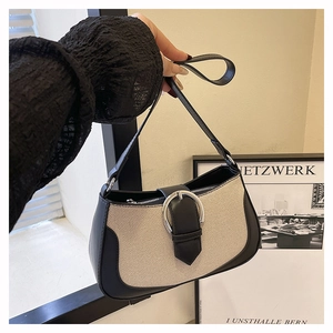 Detail of canvas and black leather shoulder bag with large silver buckle held by model