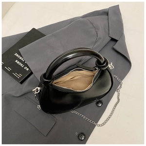 Top view of a black crescent handbag with silver chain strap on a grey suit and book